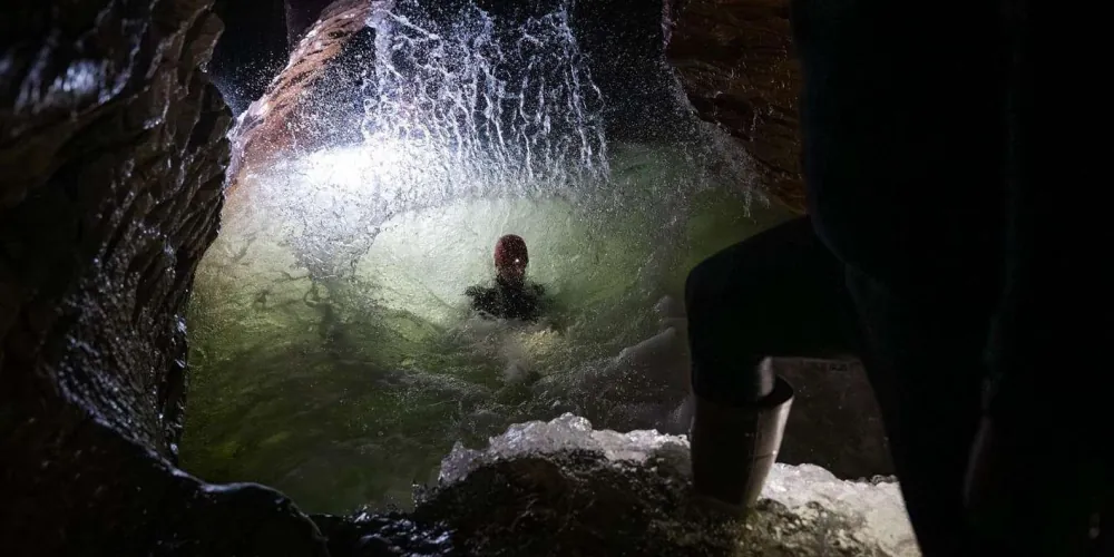 Narrow cave passage with glowworms visible above a river section
