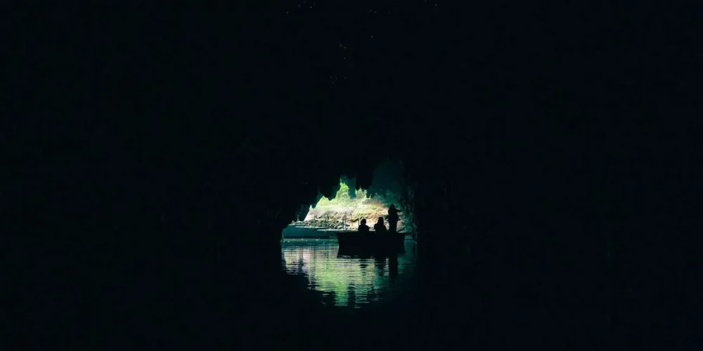 Blue-green glowworms covering a dark cave ceiling above an underground river in New Zealand